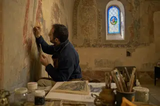 Artisan restoring a medieval fresco in a softly lit chapel, surrounded by restoration tools and archival sketches, captured in a candid moment.